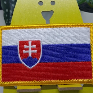 Puede incluir: Parche bordado de la bandera eslovaca. La bandera es roja, blanca y azul con el escudo de armas eslovaco en el centro. El parche tiene un borde amarillo.