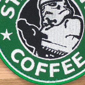 Könnte beinhalten: Gestickter Aufnäher mit dem Starbucks Coffee Logo. Das Design umfasst einen grünen Kreis mit der Starbucks-Sirene in der Mitte, umgeben von den Wörtern "COFFEE" und "STARBUCKS" in Weiß. Ein weißer Stern ist ebenfalls sichtbar.