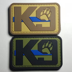 Peut inclure: Deux patchs K9 avec une empreinte de patte et une ligne bleue. Le patch du haut est beige avec un K9 et une empreinte de patte marrons. Le patch du bas est noir avec un K9 et une empreinte de patte verts.