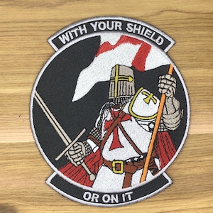Puede incluir: Parche bordado que representa a un caballero con armadura completa sosteniendo una espada y una bandera con una cruz roja. El parche es circular con el texto "WITH YOUR SHIELD" y "OR ON IT" en letras blancas.