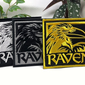 Peut inclure: Trois patchs brodés avec un motif de corbeau. Les patchs sont noirs avec des broderies blanches, noires avec des broderies grises et noires avec des broderies dorées. Chaque patch a le mot "RAVEN" brodé sous le corbeau.