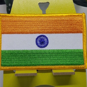 May include: An embroidered patch of the Indian flag. The flag is rectangular and features three horizontal stripes: saffron, white, and green. The white stripe has a blue wheel in the centre.