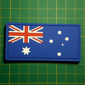 May include: A blue and white Australian flag patch with a red cross and white stars. The patch is made of a textured material and has a stitched border.