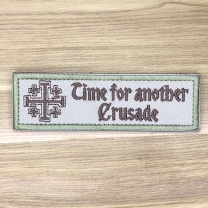 May include: Embroidered patch with a light green border and a light gray background. The patch features a Jerusalem cross on the left and the text "Time for another Crusade" in brown.