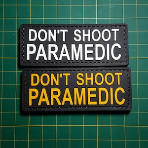 May include: Two black patches with white stitching. The top patch says "DON'T SHOOT PARAMEDIC" in white lettering. The bottom patch says "DON'T SHOOT PARAMEDIC" in yellow lettering.