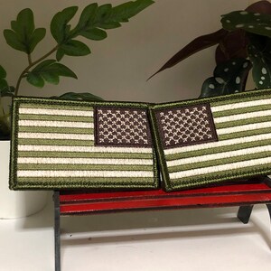 Puede incluir: Dos parches de bandera estadounidense verde y blanca con estrellas marrones. Los parches están en un pequeño banco de madera rojo.