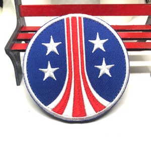 Op de afbeelding: Een blauwe en rode geborduurde patch met een wit sterrenontwerp. De patch is rond en heeft een witte rand.