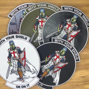 Könnte beinhalten: Gestickte Aufnäher mit einem Ritter in Rüstung, der ein Schwert und einen Schild hält. Die Aufnäher sind kreisförmig und tragen den Text "WITH YOUR SHIELD" oder "OR ON IT". Die Rüstung des Ritters hat rote Kreuze und blaue Akzente.