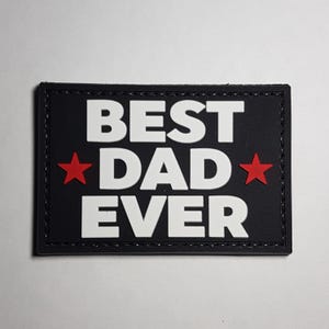Può includere: Toppa nera con testo bianco che recita "BEST DAD EVER" con una stella rossa su entrambi i lati della parola "DAD".