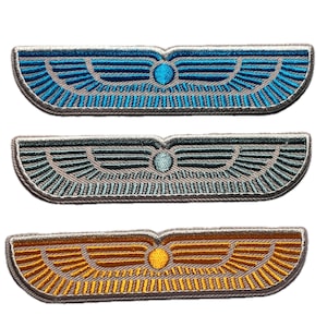 May include: Three embroidered wing-shaped patches. The top patch is blue, the middle is teal, and the bottom is gold. Each patch features a central circular detail and intricate wing patterns.