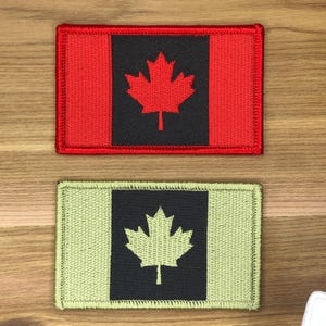 Puede incluir: Dos parches rectangulares con la bandera canadiense. El parche superior tiene un borde y un campo rojos, una sección central negra y una hoja de arce roja. El parche inferior tiene un borde y un campo verdes, una sección central negra y una hoja de arce verde.
