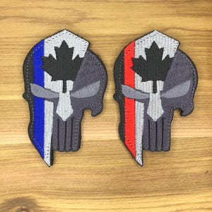 May include: Two embroidered patches in the shape of a skull. One patch features blue, white, and gray stripes, and the other has red, white, and gray stripes. Both patches have a black maple leaf.