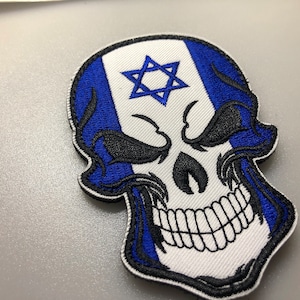 Könnte beinhalten: Ein blauer und weißer Totenkopf-Patch mit einem Davidstern auf der Stirn. Der Schädel ist schwarz umrandet und hat ein weißes Lächeln.