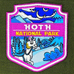 Op de afbeelding: Geborduurde patch met een schildontwerp. De patch toont een besneeuwde berglandschap met een wit, lama-achtig wezen, blauwe bomen en de tekst "HOTH NATIONAL PARK" in geel en wit. De rand is roze en wit.