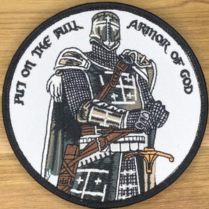 May include: Embroidered patch featuring a medieval knight in full armor, holding a sword. The design includes the text "PUT ON THE FULL ARMOR OF GOD" in a circular pattern around the knight. The patch has a black border.