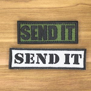 Può includere: Due toppe rettangolari con la scritta "SEND IT". Una toppa ha testo nero su sfondo verde con bordo nero. L'altra ha testo nero su sfondo bianco con bordo nero.