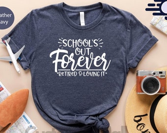 May include: Heather navy t-shirt with the text "SCHOOL'S OUT FOREVER RETIRED & LOVING IT". The image includes a straw hat, a camera, a map, a passport, and a pair of brown shoes. The shirt is available in 10+ colors.