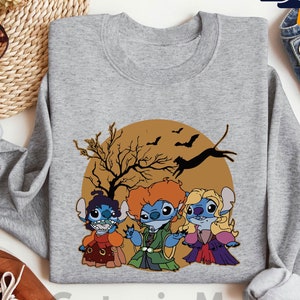 Puede incluir: Una sudadera gris con un dise&ntilde;o tem&aacute;tico de Halloween. El dise&ntilde;o presenta tres personajes de dibujos animados disfrazados de brujas frente a un c&iacute;rculo marr&oacute;n con un &aacute;rbol, murci&eacute;lagos y un gato negro. El texto "CustomizeMall" est&aacute; en la parte inferior.