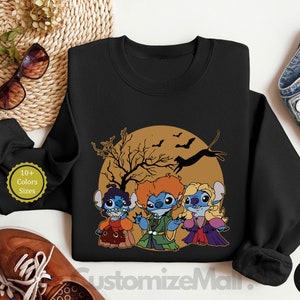 Puede incluir: Sudadera negra de cuello redondo con un dise&ntilde;o de Halloween que presenta tres personajes de dibujos animados disfrazados, ambientados contra una luna llena con murci&eacute;lagos y un &aacute;rbol. El texto "10+ Colors Sizes" es visible.