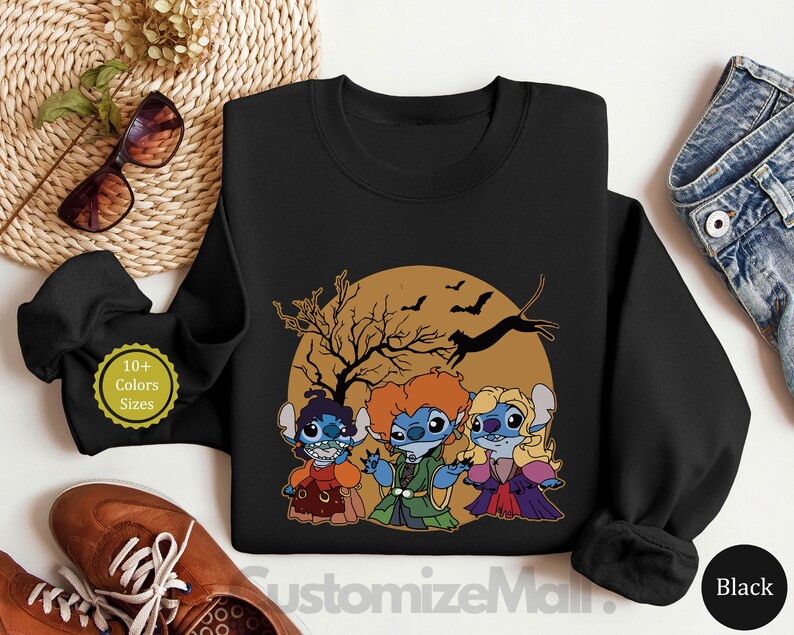 Puede incluir: Sudadera negra de cuello redondo con un dise&ntilde;o de Halloween que presenta tres personajes de dibujos animados disfrazados, ambientados contra una luna llena con murci&eacute;lagos y un &aacute;rbol. El texto "10+ Colors Sizes" es visible.