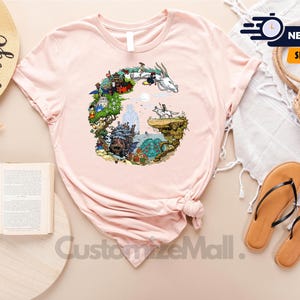 a pink t-shirt with a colorful graphic design, a straw hat, a book, a pair of sandals, and a woven basket, all arranged on a light-colored surface.