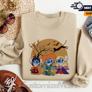 Puede incluir: Sudadera de color arena con un gr&aacute;fico de Halloween que representa a tres personajes de dibujos animados disfrazados de brujas, con una luna llena, murci&eacute;lagos y una silueta de &aacute;rbol desnudo. El texto "CustomizeMall" est&aacute; en la parte inferior.