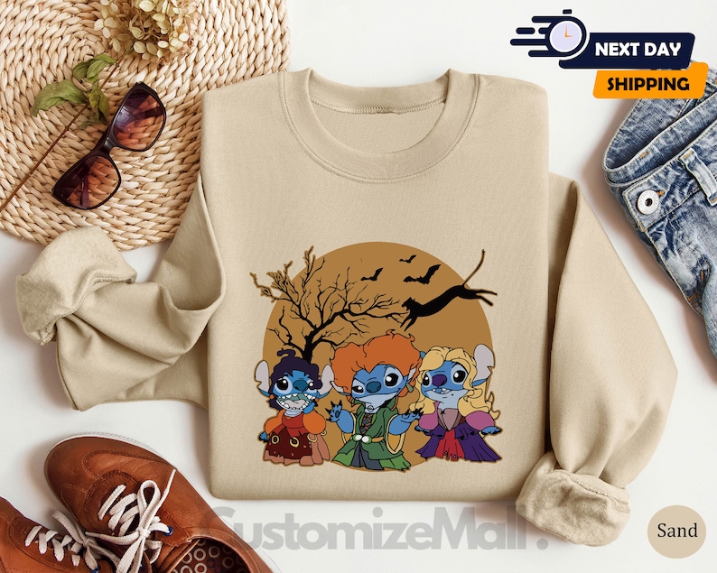 Puede incluir: Sudadera de color arena con un gr&aacute;fico de Halloween que representa a tres personajes de dibujos animados disfrazados de brujas, con una luna llena, murci&eacute;lagos y una silueta de &aacute;rbol desnudo. El texto "CustomizeMall" est&aacute; en la parte inferior.