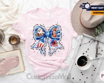 May include: Pink t-shirt with a blue bow and red, white, and blue stars and stripes. The bow has an American bald eagle and the text "Happy 4th of July" repeated around the bow.