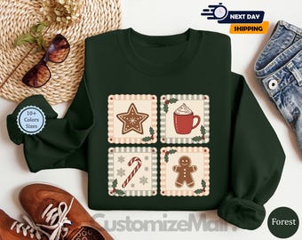 May include: A dark green sweatshirt featuring four square designs with Christmas-themed illustrations. The designs include a gingerbread star, a mug of hot cocoa, a candy cane, and a gingerbread man. The sweatshirt has the text "CustomizeMain" at the bottom.