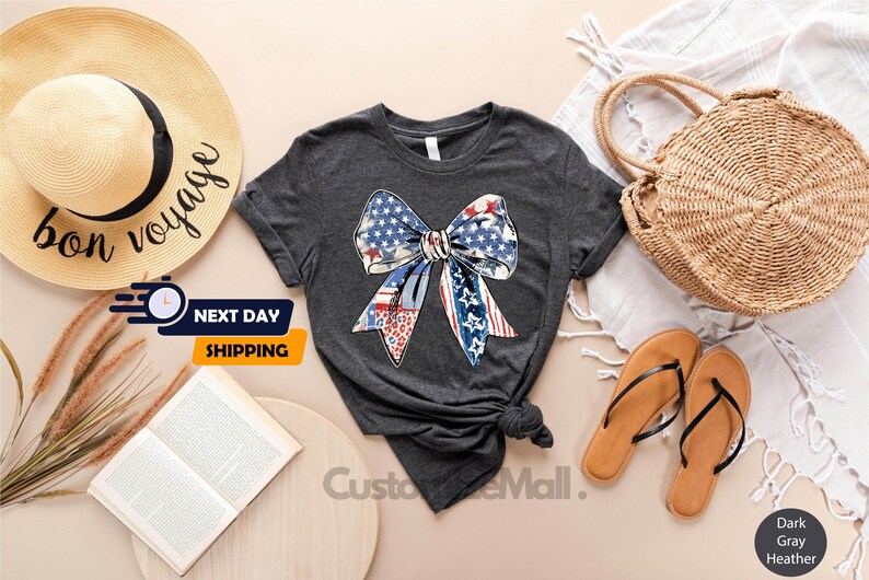 May include: A dark gray t-shirt with a red, white, and blue bow made of American flag fabric. The bow is centered on the shirt.