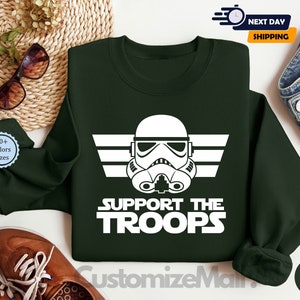 May include: A dark green sweatshirt with a white graphic of a Star Wars Stormtrooper helmet and the text "Support the Troops".