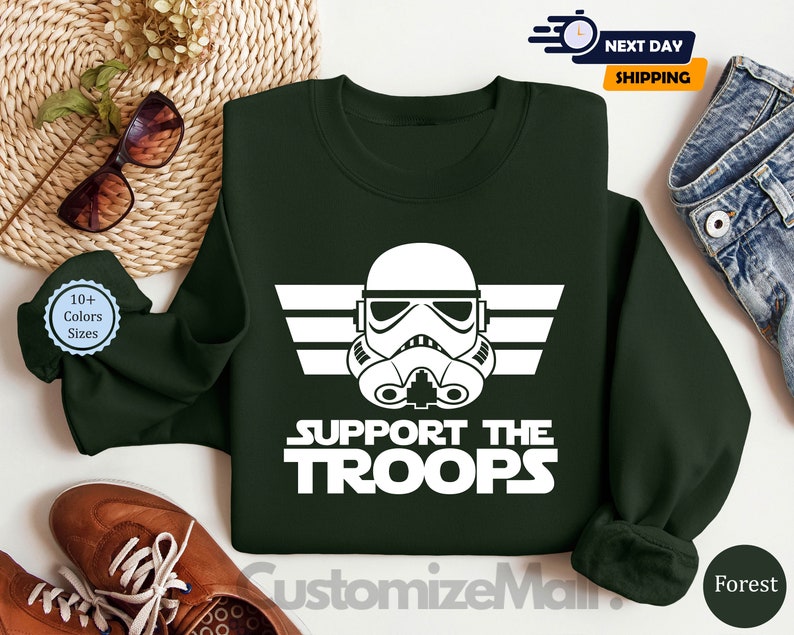 May include: A dark green sweatshirt with a white graphic of a Star Wars Stormtrooper helmet and the text "Support the Troops".