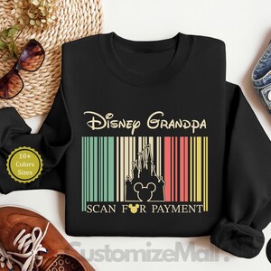a black sweatshirt with a Disney Grandpa design, a pair of sunglasses, a pair of brown shoes, and a pair of jeans, all laid out on a white background.