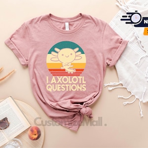 May include: A pink t-shirt featuring a retro-style graphic of an axolotl with the text "I axolotl questions".