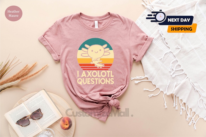 May include: A pink t-shirt featuring a retro-style graphic of an axolotl with the text "I axolotl questions".