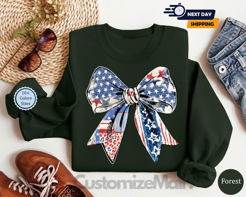 May include: A dark green sweatshirt with a large red, white, and blue bow with stars and stripes. The bow is in the center of the sweatshirt. The sweatshirt is on a white surface.