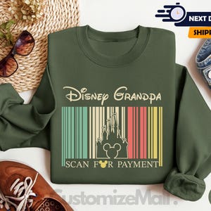 a green sweatshirt with a Disney Grandpa design, a pair of sunglasses, a woven basket, a pair of brown shoes, and a pair of jeans, all arranged on a white background.