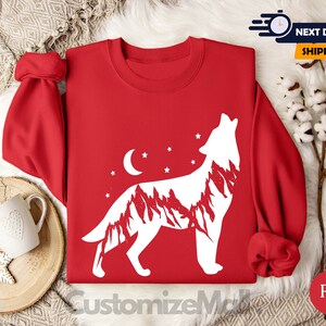 K&ouml;nnte beinhalten: Ein rotes Sweatshirt mit einem wei&szlig;en Design eines heulenden Wolfs, das eine Bergketten-Silhouette, einen Mond und Sterne enth&auml;lt. Der Text "CustomizeMall" ist unten sichtbar.