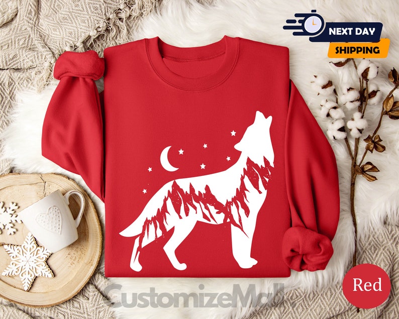 K&ouml;nnte beinhalten: Ein rotes Sweatshirt mit einem wei&szlig;en Design eines heulenden Wolfs, das eine Bergketten-Silhouette, einen Mond und Sterne enth&auml;lt. Der Text "CustomizeMall" ist unten sichtbar.