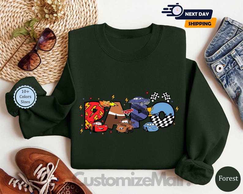 Puede incluir: Una sudadera de color verde oscuro con un gr&aacute;fico de los personajes de Cars, incluyendo Rayo McQueen, Mate y otros. El gr&aacute;fico est&aacute; en un estilo de dibujos animados colorido e incluye la palabra "RACO" en una fuente estilizada.