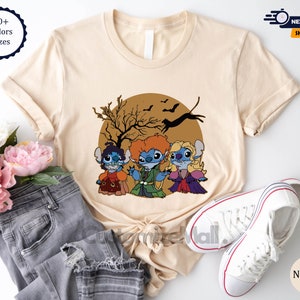 Puede incluir: Camiseta beige con una ilustraci&oacute;n de dibujos animados de tres personajes de Stitch vestidos como las hermanas Sanderson de Hocus Pocus, sobre una luna marr&oacute;n con murci&eacute;lagos y un &aacute;rbol. La camiseta incluye el texto "10+ Colors Sizes" y "Natural".