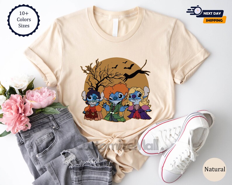 Puede incluir: Camiseta beige con una ilustraci&oacute;n de dibujos animados de tres personajes de Stitch vestidos como las hermanas Sanderson de Hocus Pocus, sobre una luna marr&oacute;n con murci&eacute;lagos y un &aacute;rbol. La camiseta incluye el texto "10+ Colors Sizes" y "Natural".