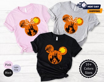 May include: Pink, light gray, and black t-shirts featuring a Halloween-themed design. The design is a silhouette of a castle, bats, and a full moon inside a Mickey Mouse head shape. The shirts are available in 10+ colors and sizes.