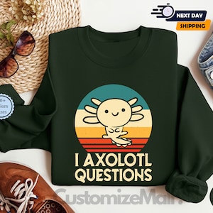 May include: A dark green sweatshirt featuring a retro-style illustration of an axolotl. The axolotl is yellow and has a pink nose. The text "I axolotl questions" is printed below the illustration.