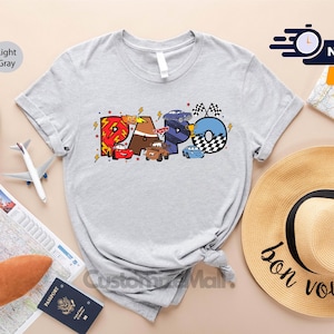Może przedstawiać: Jasnoszary t-shirt z kolorową grafiką kresk&oacute;wek samochod&oacute;w, kt&oacute;re tworzą słowo "RAPO".