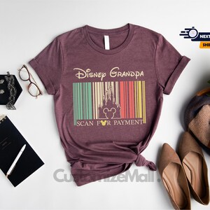 a purple t-shirt with a Disney Grandpa design, along with various accessories such as a notebook, a pen, a pair of glasses, and a bouquet of flowers.