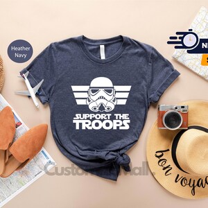 May include: A navy blue t-shirt with a white graphic of a Star Wars Stormtrooper helmet with wings and the text "Support the Troops".