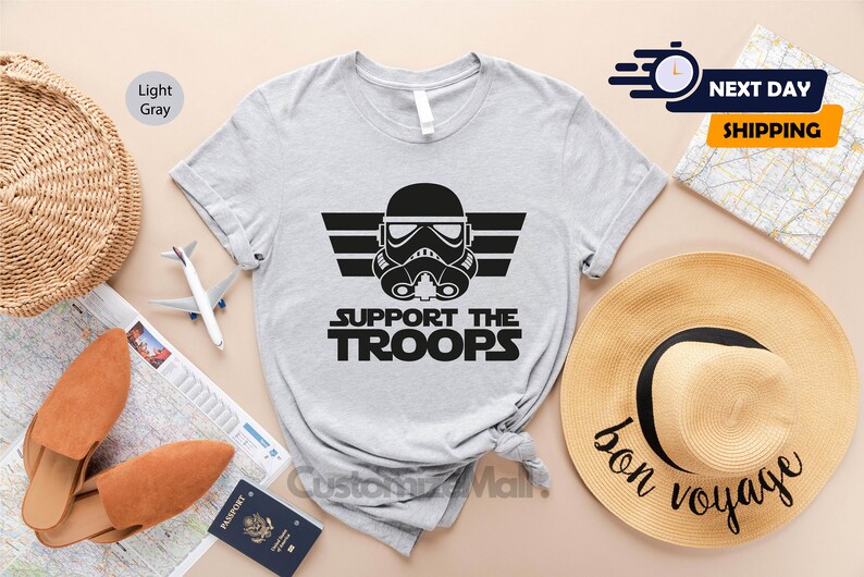 May include: Light gray t-shirt with a black graphic of a Star Wars Stormtrooper helmet with the text "Support the Troops" underneath.
