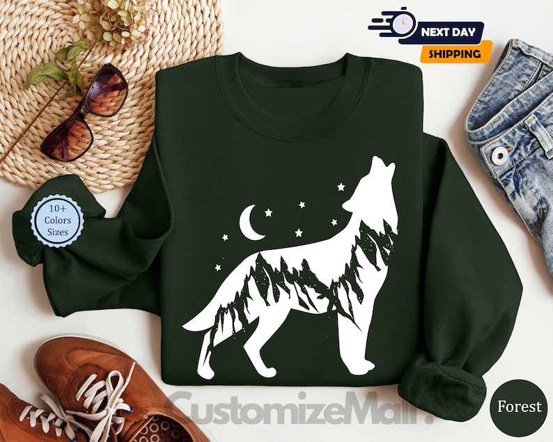 K&ouml;nnte beinhalten: Dunkelgr&uuml;nes Sweatshirt mit einer wei&szlig;en Wolfsilhouette, die Mond und Sterne anheult. Der K&ouml;rper des Wolfes ist mit einem Bergketten-Design gef&uuml;llt. Das Sweatshirt hat einen Rundhalsausschnitt und lange &Auml;rmel. Der Text "CustomizeMain" ist unten sichtbar.