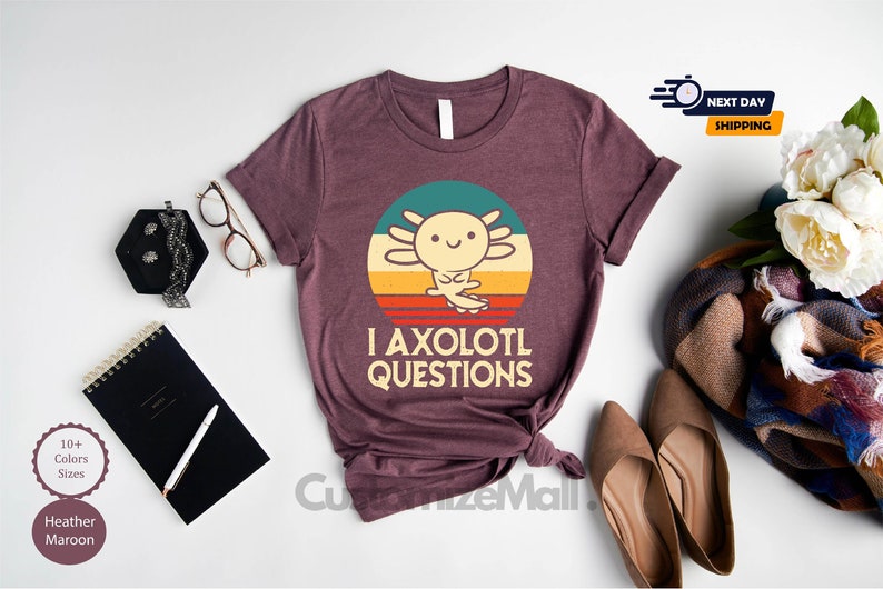 May include: A heather maroon t-shirt featuring a retro-style graphic of an axolotl with the text "I axolotl questions".